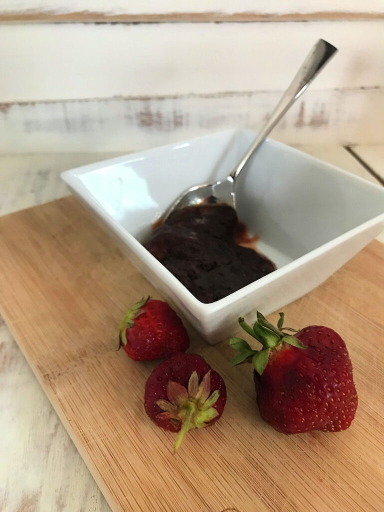 jam and spoon in small bowl with strawberries near it