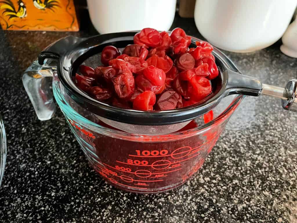 straining cherries over a measuring cup
